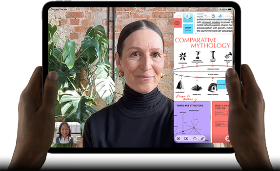 Vooraanzicht van iPad Pro, horizontale stand, kleur spacezwart, afgeronde hoeken, zwarte rand rond het display, handen houden de linker- en rechterkant vast, display toont een FaceTime-gesprek dat live wordt vertaald en een educatieve app met een presentatie van ‘Comparative Mythology’ met tekst, diagrammen en handgeschreven notities