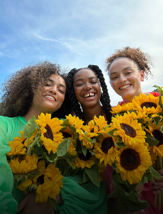 Een scherpe en kleurrijke selfie van drie mensen die bloemen vasthouden.